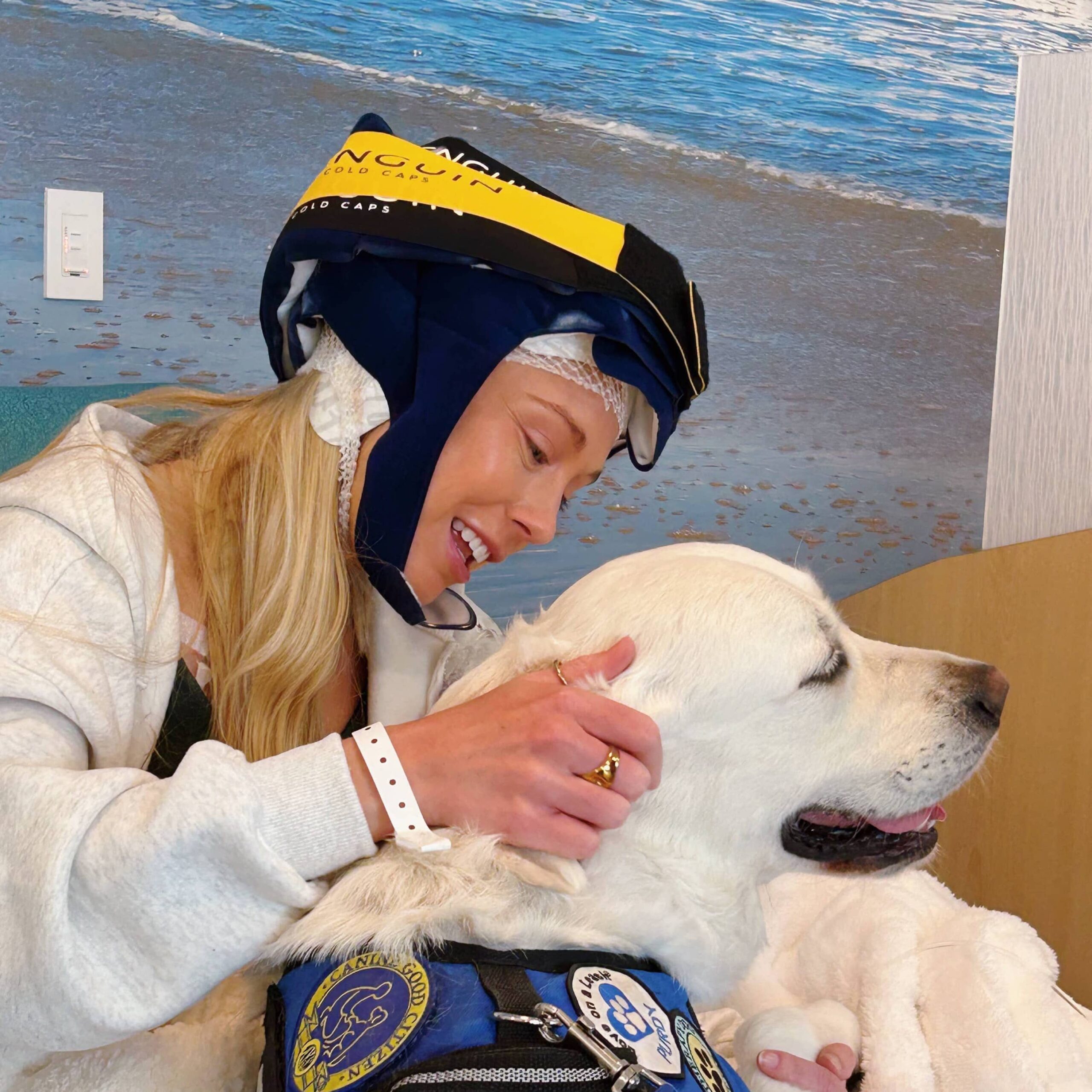 Tanner wearing a Penguin Cold Cap during chemotherapy, smiling and petting a therapy dog.