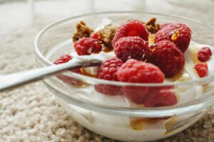 Bowl of yoghurt topped with raspberries and honey with a spoon.